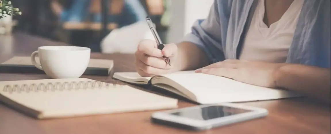 A person at their desk with their notebook, planner, and phone.