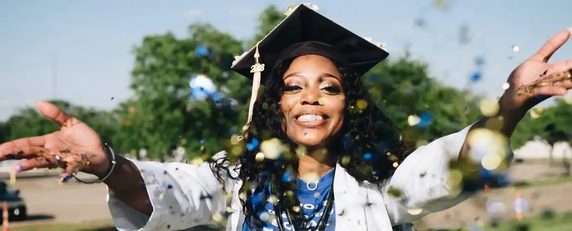A woman in a graduation cap and gown throwing confetti