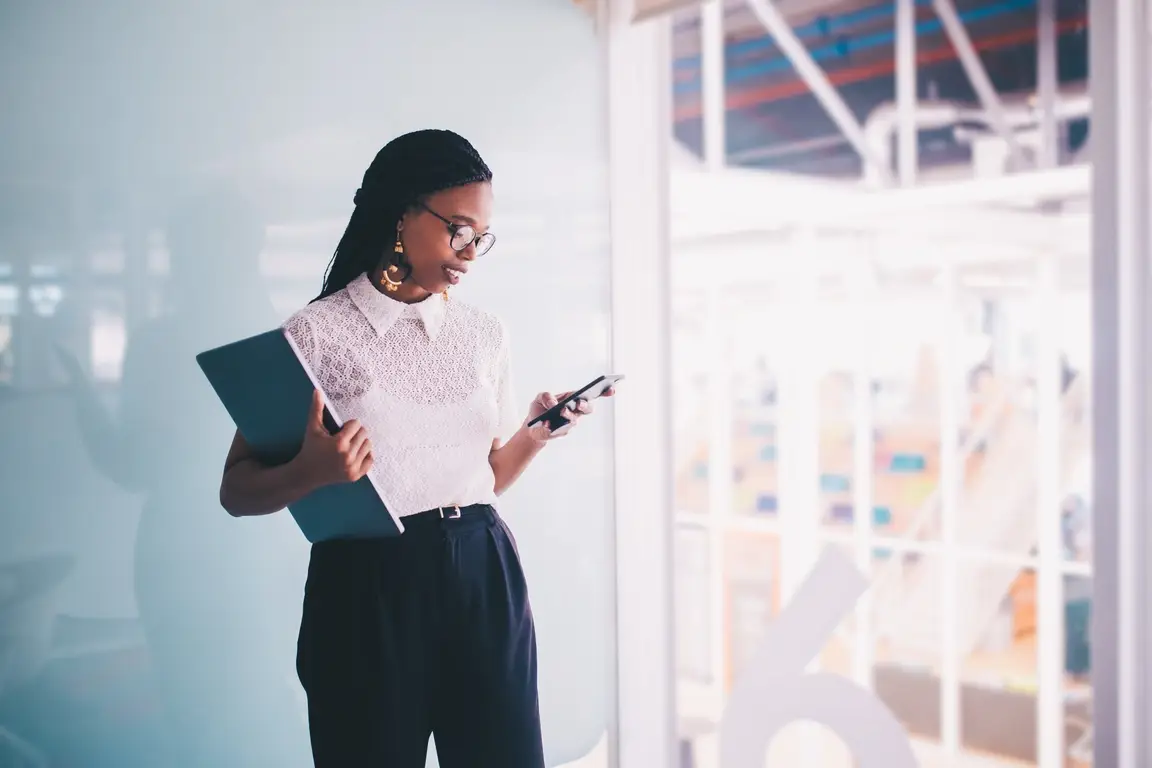 A woman in an office holding a laptop and a mobile phone.