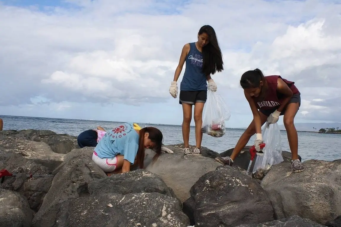 Three young people with garbage bags scavenge for litter on the beach.
