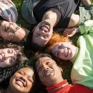 Grupo de personas acostadas en el pasto en círculo sonriendo