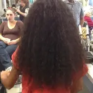 Imagem de uma mulher sentada de costas, com os cabelos longos e castanho-escuros em destaque.