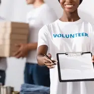 Volunteer smiles while holding out a sign-up form at a nonprofit organization.