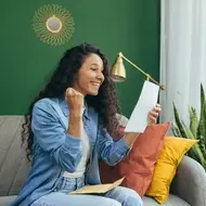 Girl with long dark, curly hair celebrates a grad school acceptance letter on her couch at home.