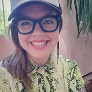 A woman wearing a cap and black glasses smiling