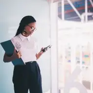 Uma mulher em um escritório segurando um laptop e um celular.