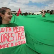 A luta pelas florestas começa na rua - poster segurado por uma mulher vestindo junto com outras pessoas um pano verde contínuo, como se fosse uma floresta