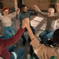 Personas sentadas en círculo con las manos unidas y elevadas.