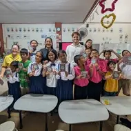 Estudiantes de una clase con personas voluntarias mostrando sus pasaportes de aprendizaje