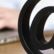 Uma fotografia de um sinal de internet @ na frente de alguém digitando em um laptop.