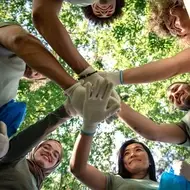 a group of co-workers volunteer together and put their hands together after completing their volunteer opportunity cleaning up a local park