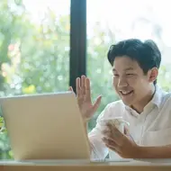 young man waves at camera on laptop while smiling