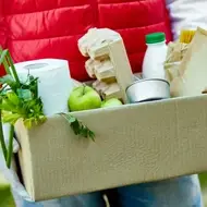 Volunteer brings groceries to someone in need, carrying a cardboard box of food and cleaning supplies.