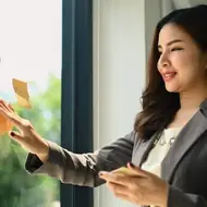 Woman puts sticky notes on a window at her office, smiling on a sunny day.