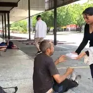 Una persona entrega comida a una persona habitante de calle.
