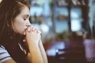 A young woman with her eyes closed and her hands clasped to her mouth.