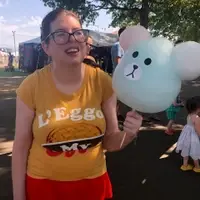 Amy is holding a teddy bear balloon at the fair.