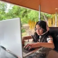 young latina girl focused in her online English class wearing headset and sitting in a covered area outside