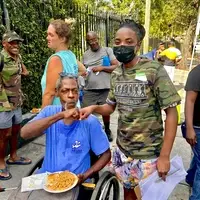 REAL AMERICANS CORPORATION volunteer engaging with a community member using a wheelchair during a food and essential-aid outreach event in Miami.
