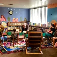 A group of young children and adults sitting in front of a woman reading a book