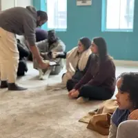 A brother serve tea to event attendees sitting in a circle on the floor