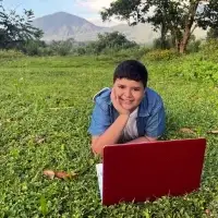 boy in El Salvador laying down on grass with his red laptop with nature around him