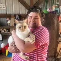 Leslie is holding a cat in a barn.
