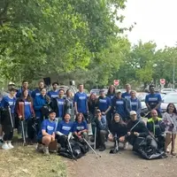 A group of people in blue t-shirts with litter picks posing together.