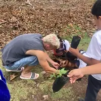 A Semillas Life volunteer and local primary school students working together to plant native trees in Codo del Pozuzo, Peru. The image captures a hands-on environmental education lesson where children are learning reforestation techniques in the Amazon rainforest.