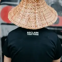 A person wearing a cedar hat and a black tshirt with the words reclaim your power stands with their back to the camera
