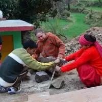 A volunteer and two villagers set stones in place on a building site.