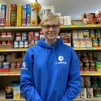 Smiling AmeriCorps Member in front of shelves of canned good at the food pantry