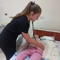 A medical intern at Semillas Life NGO using a stethoscope to perform a lung examination on a local child at a rural health center in Codo del Pozuzo, Peru. The intern is focused on the patient, demonstrating hands-on clinical experience in an Amazonian community.