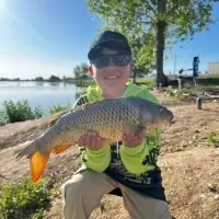 A young boy poses with a big fish at the side of a lake.