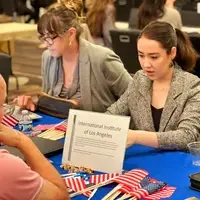 two women sit at computers at a table with a sign that reads "International Institute of Los Angeles"