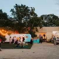 Evening at a warehouse artspace, with lighted trailers and clusters of people socializing