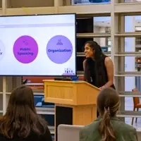 a Serve VISTA member smiles at a podium with a presentation screen behind her