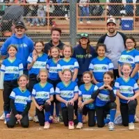 A girls' softball team smiles and poses in team jerseys with their volunteer coaches.