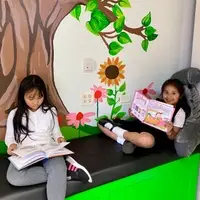 Two young girls reading books on a new bench under a mural of a tree and flowers.