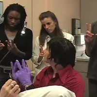 A GTA demonstrates hand positions to three medical students, all holding up two fingers.