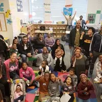 Room full of Black families with lots of young children and their parents, uncles, aunts and friends.