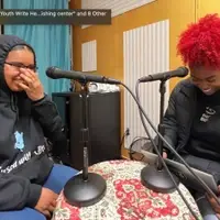 Two brown teens in black hoodies laughing at microphones