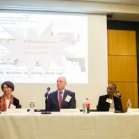 Four people seated next to one another on a panel with a projected presentation behind them showing a slide about gun violence as a public health issue.