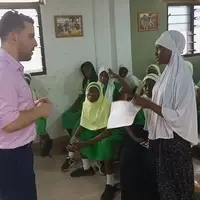 Ian Thomson, a law and human rights intern from Gonzaga University, Spokane, engaging with a group of Achievers girls in Nima, Accra, Ghana. The discussion focuses on human rights awareness and women’s empowerment, highlighting issues such as gender equality, access to education, and personal development. The girls are actively participating, asking questions and sharing their experiences, while Ian guides the conversation and provides insights based on his training. The session takes place in an open community space, with colorful walls and educational posters in the background. Local volunteers and Pro-Passion Projects coordinators are present, supporting the interactive session and documenting the impact. Everyone is attentive and engaged, reflecting the collaborative effort to empower young women through knowledge, mentorship, and advocacy for human rights in Nima, Accra."