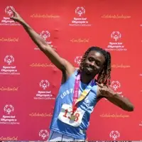 An athlete from Special Olympics Northern California proudly stands in front of the winners podium, holding their medal with a bright smile, embodying determination and achievement.