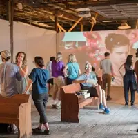 Crowds socializing during an art opening of video projection work in a warehouse artspace