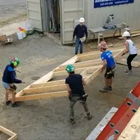 Four young adults lifting a wooden wall frame on a construction site