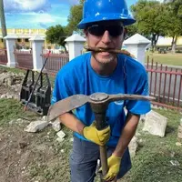 National service member, in a blue shirt holding a pick-mattock digging tool.