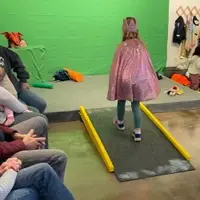 A girl is walking up a ramp towards a green screen while adults watch her performance on stage