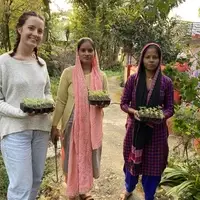 Three women hold trays of young plants.